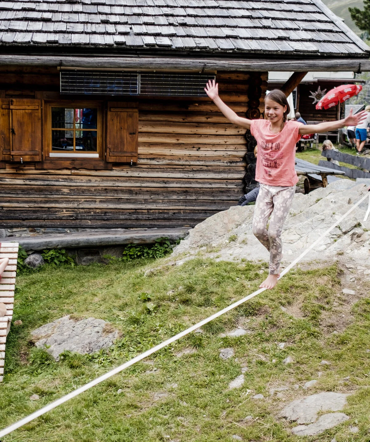 Zwei Kinder balancieren auf einem Seil, das vor einer Berghütte gespannt ist | © DAV/Hans Herbig