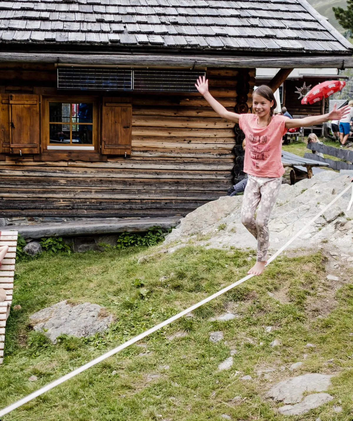 Zwei Kinder balancieren auf einem Seil, das vor einer Berghütte gespannt ist | © DAV/Hans Herbig