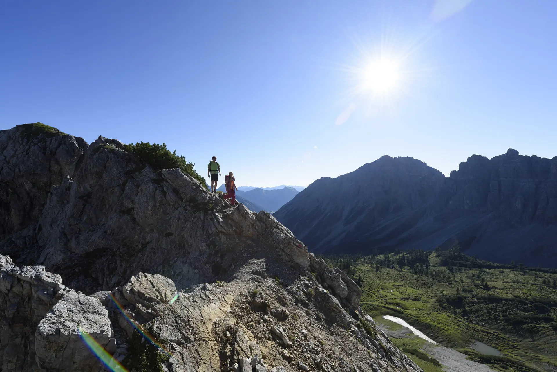 Zwei Wanderer auf einem Felsgrat. Im Hintergrund grüne Bergwiesen | © DAV / Wolfgang Ehn